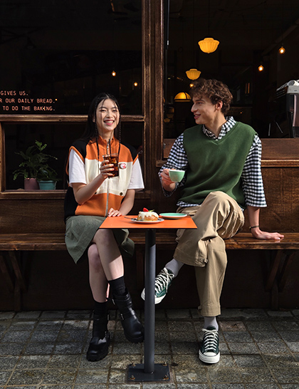 Sytě barevná fotografie dvou lidí sedících před kavárnou pořízená s 2násobným přiblížením.