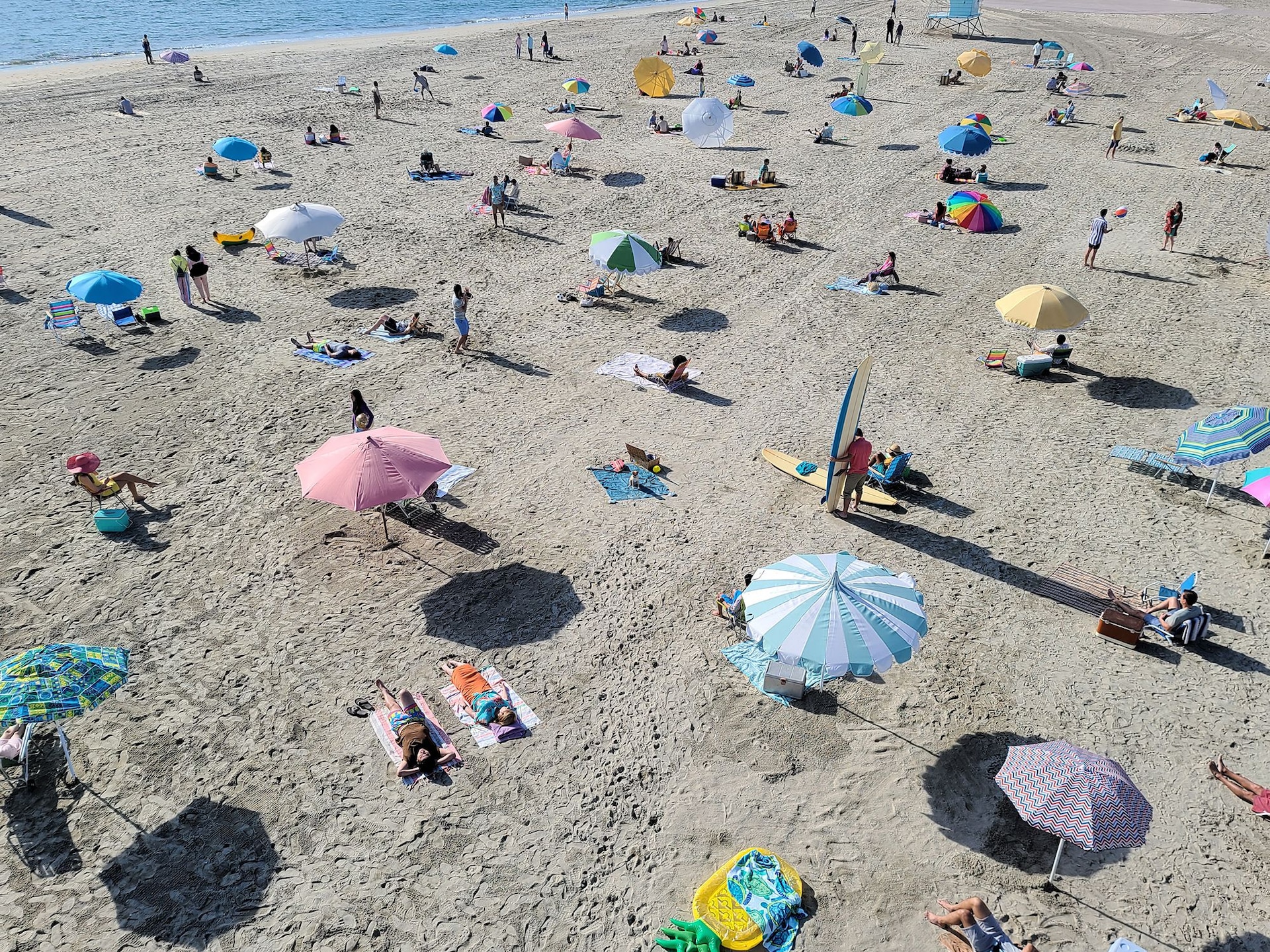 Ein Foto eines Strandes mit vielen Menschen, das mit dem Galaxy S20 Ultra 5G aufgenommen wurde. Wenn wir hereinzoomen, sehen wir einen Hund, der auf einem Badetuch sitzt und eine rosafarbene Sonnenbrille trägt. Damit wird deutlich, das man mit Space Zoom Momente erleben kann, die man andernfalls nicht gesehen hätte. 