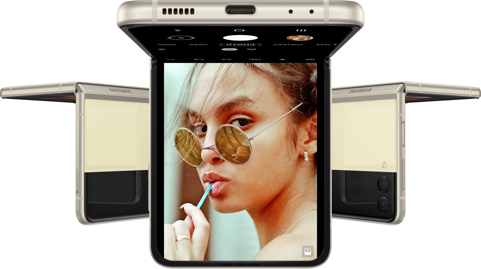 Drei Galaxy Z Flip3 5G Smartphones im Flex-Modus und auf dem Kopf stehend. Auf dem nach vorne gerichteten Smartphone ist die Kamera-App auf dem Hauptdisplay zu sehen und eine Frau, die in die Kamera blickt.