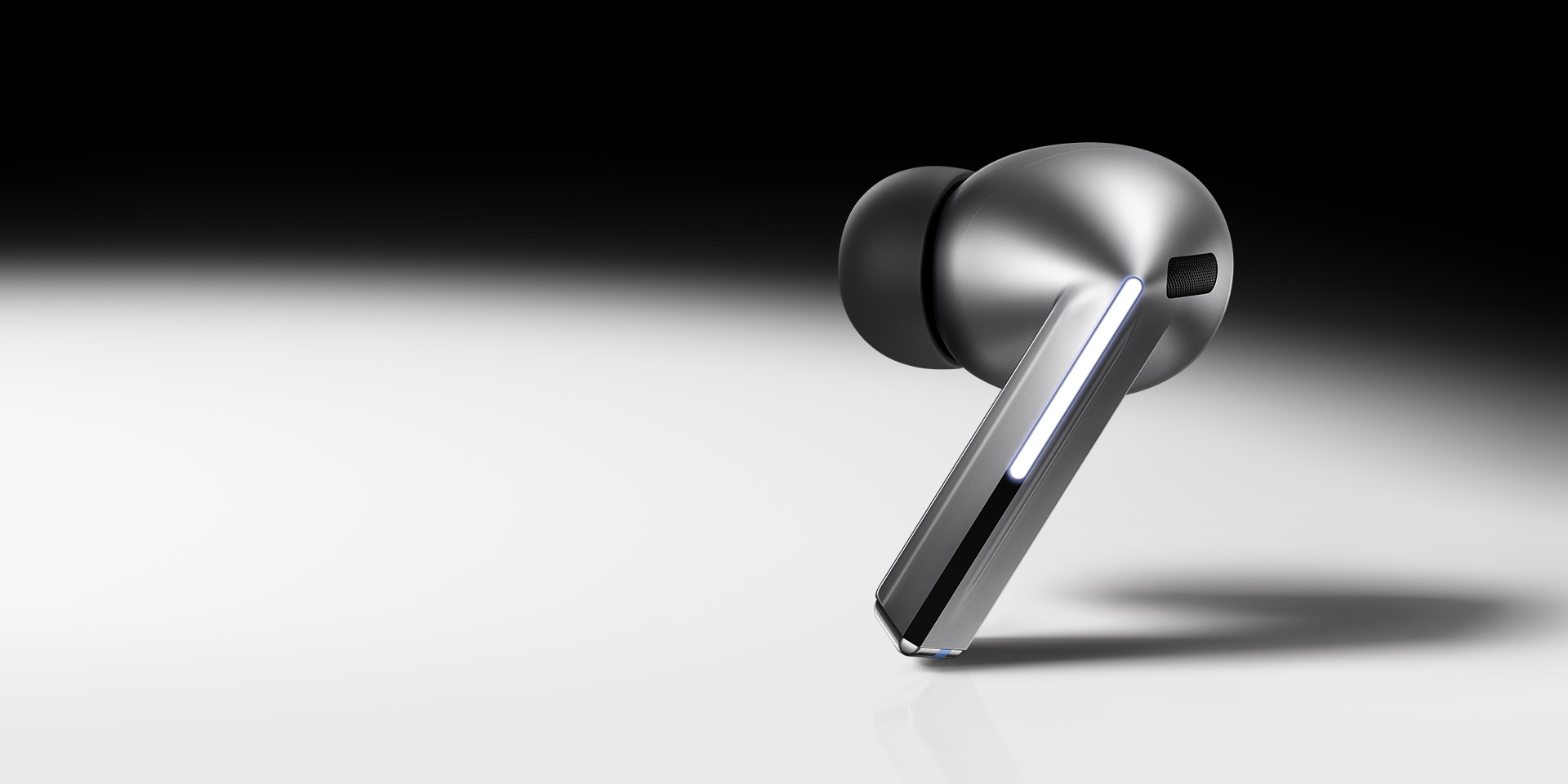 En enkelt, sølvfarvet Galaxy Buds3 Pro høretelefon på en gradueret sort-hvid baggrund.
