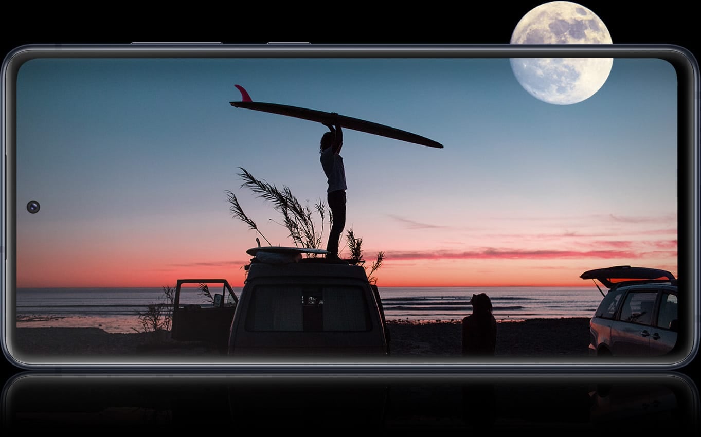 Galaxy S20 FE con una fotografía nocturna en la pantalla que muestra una sombra de una persona que sostiene una tabla de surf sobre su cabeza. En el cielo brilla una luna llena. La luna llena está medio fuera de la pantalla, lo que representa la autonomía de la batería durante todo el día que está disponible en el Galaxy S20 FE. 