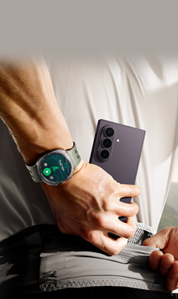 Un hombre se guarda un Galaxy Z Fold8 Ultra en Violeta Nocturno en un bolsillo. En la muñeca lleva un Galaxy Watch Ultra2 en Gris Titanio. Aparece el menú de entrenamiento Trail Run en la pantalla del reloj.