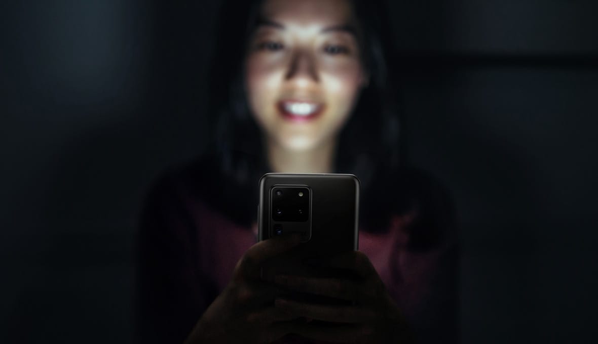 Une femme utilisant son Galaxy S20 Ultra et souriante car elle est rapide et puissante avec le point d'accès et la RAM avancés