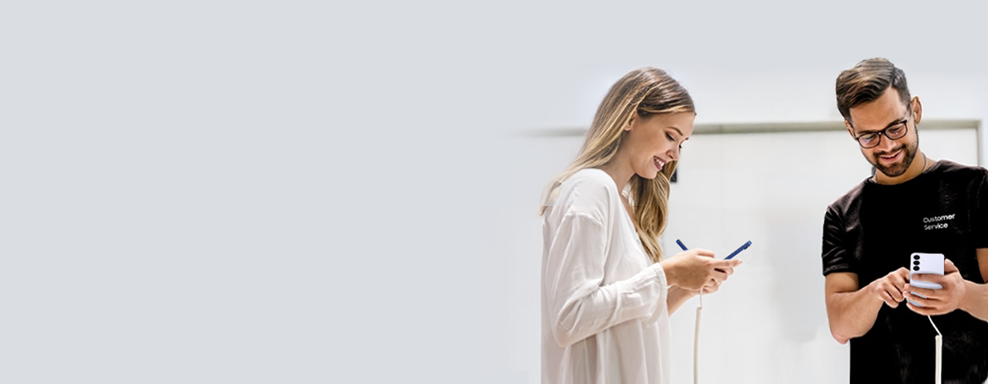 Une femme en blouse blanche et un homme en chemise noire sourient et regardent leurs téléphones Samsung.