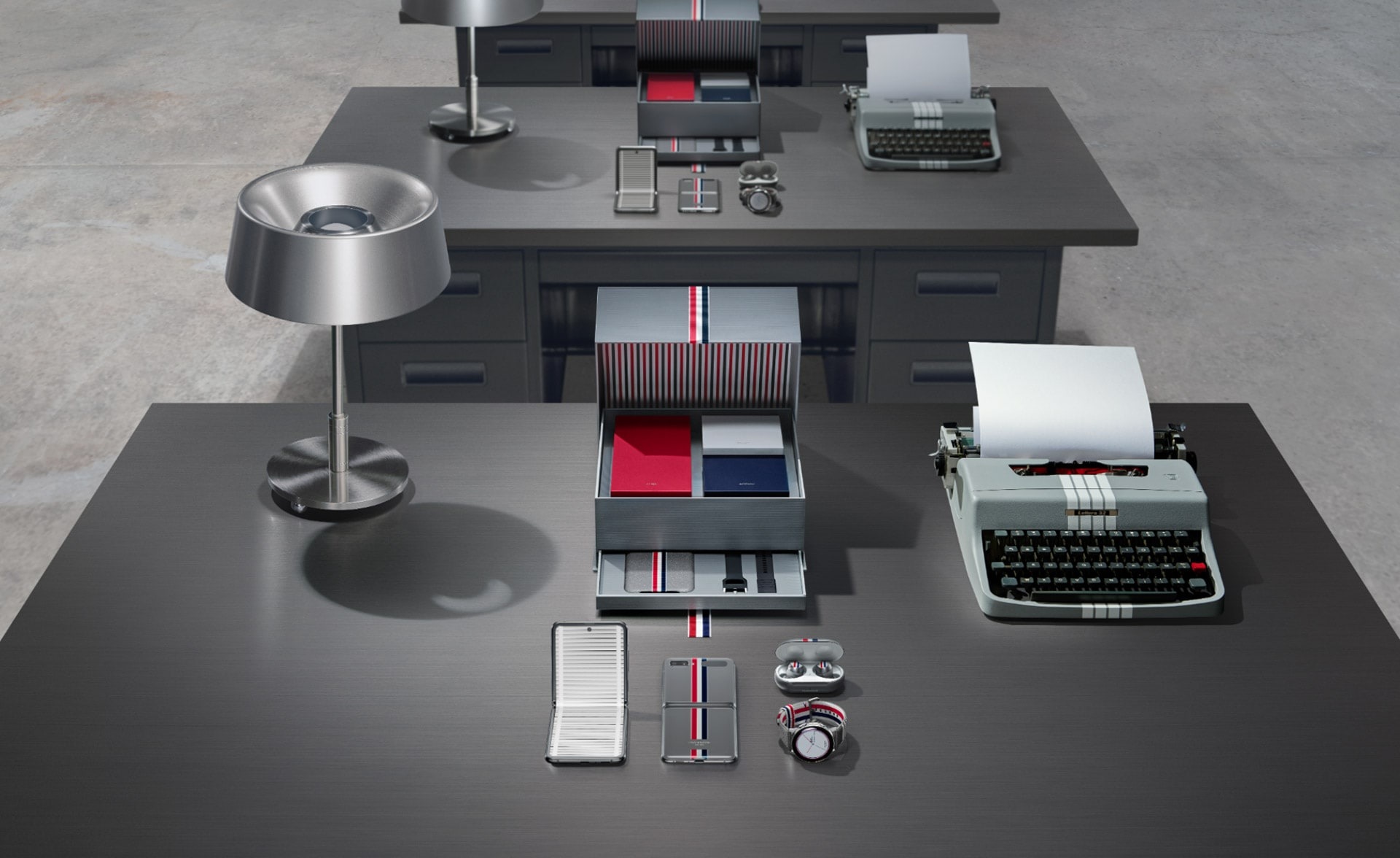 Le Galaxy Z Flip édition Thom Browne, image montrant la collection sur un bureau avec une machine à écrire et une lampe en acier. L'écrin est ouvert et révèle à l'intérieur, l'édition spéciale du Galaxy Z Flipn les Galaxy Buds plus, la Galaxy Watch Active2, l'étui en cuir et les bracelets pour la Galaxy Watch Active2.