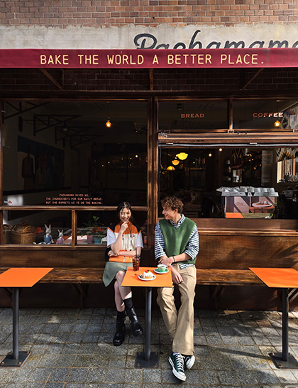 Ein farbintensives Foto von zwei Personen, die vor einem Café sitzen, aufgenommen mit 1-fachem Zoom.