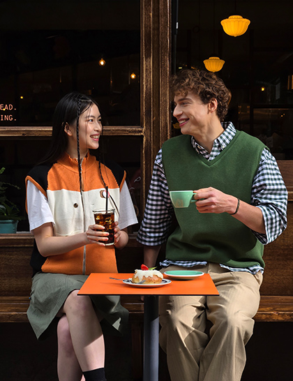 Uma foto colorida de duas pessoas sentadas em frente a um café, tirada com zoom de 3x.
