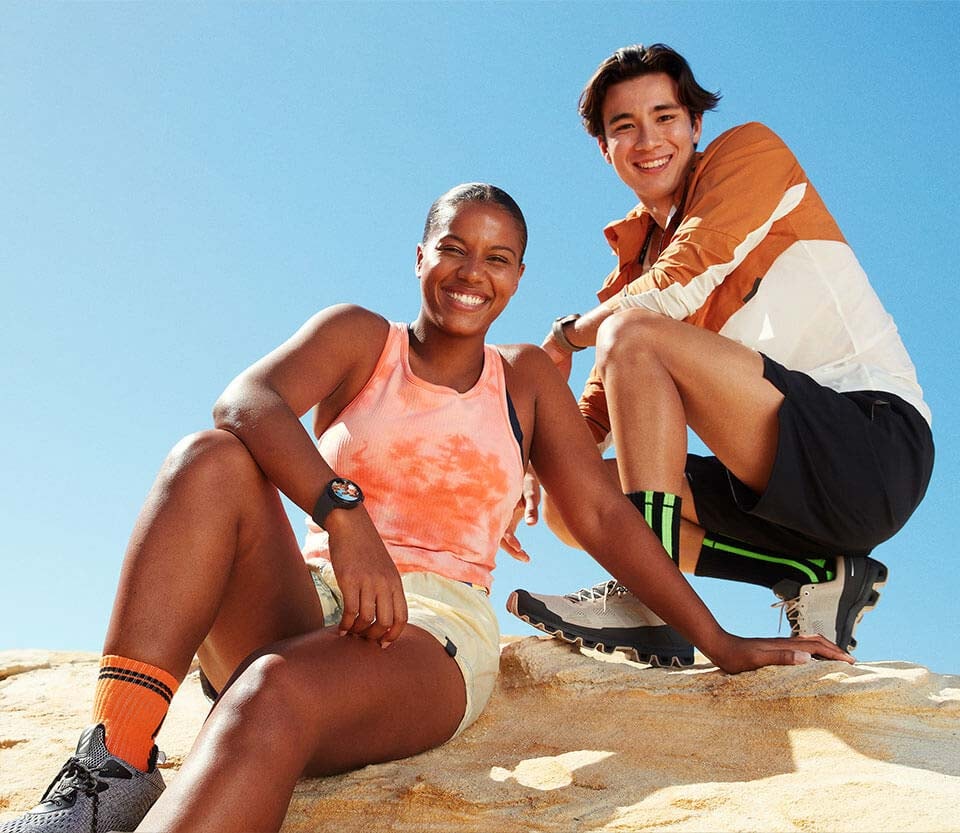 A man and a woman smiling while taking a low-angle photo using the Galaxy Watch5 Pro to control their smartphone camera. Both of them are wearing Galaxy Watch5 Pro on their wrists.