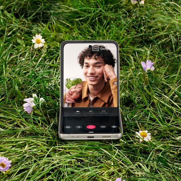 Samsung Flip 3 5G dalam mode Flex di tengah lapangan dengan panggilan video di layar. Orang di seberang telepon adalah seorang pria yang sedang memegang minuman.