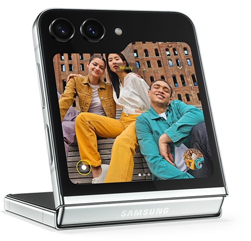 A preview of a selfie is displayed on the Flex Window of Galaxy Z Flip5 in Flex Mode. Three friends pose together for the selfie taken at a distance away from the device.