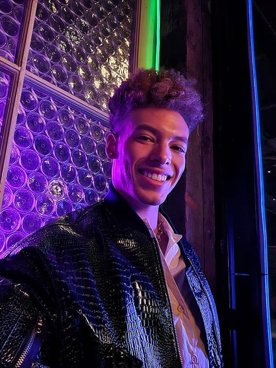 A man takes a selfie at a dark venue with coloured lights. His face is bright and colours are vivid. The photo was taken with Galaxy S23 plus using wide mode with an aperture of F 2.2.