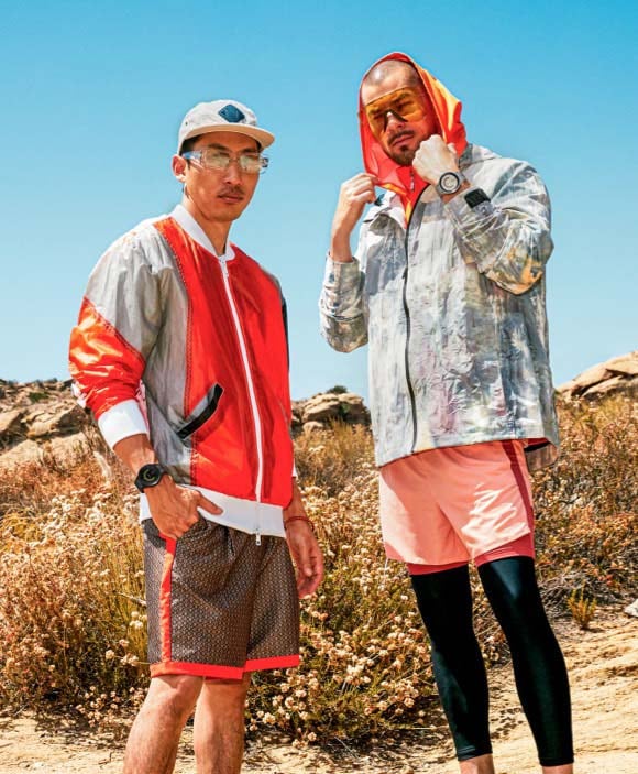 שני גברים מדגמנים בחוץ בבגדי טיולים כתומים בסגנון אורבני, כשעל מפרקי כפות ידיהם שעוני Watch5 Pro.