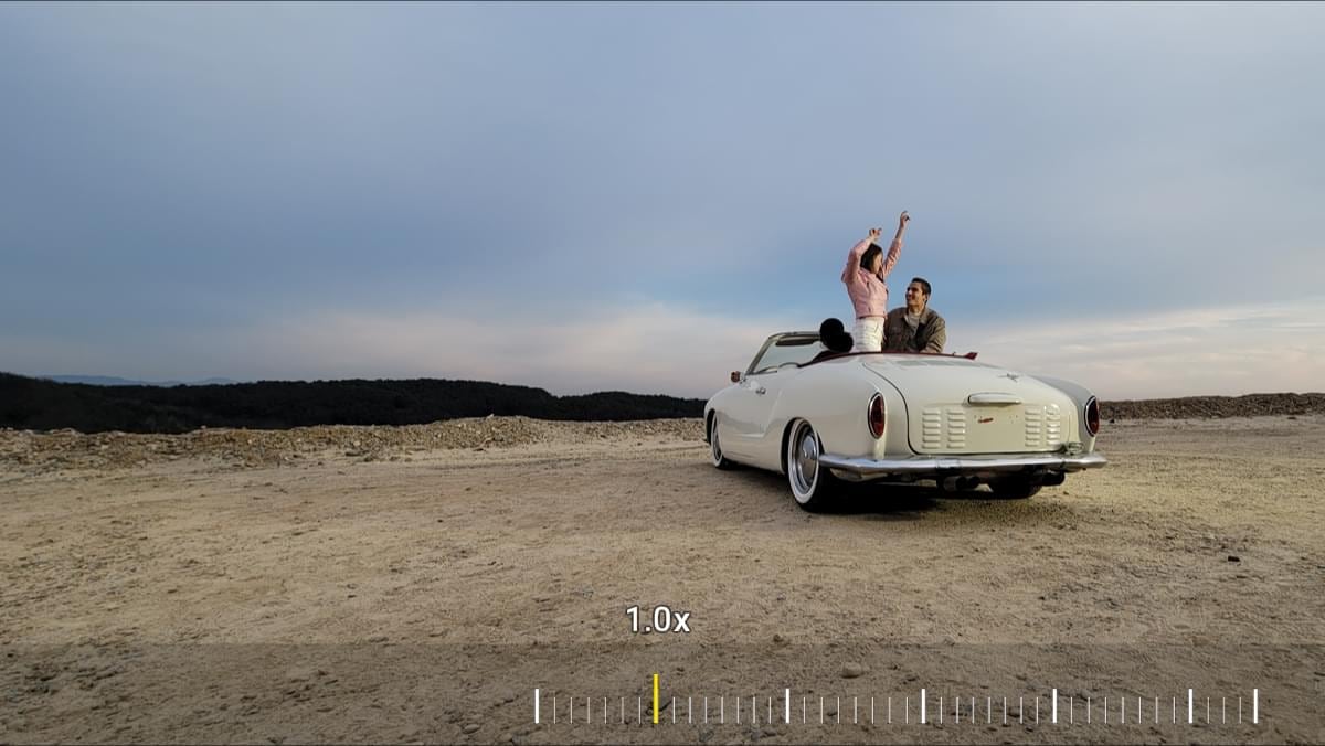Car with a couple in the back seat. As you zoom in, you see someone in the driver's seat. As you zoom in all the way to 30x, you see her smiling expression through the sideview mirror.