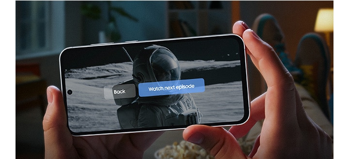 Two hands hold a Galaxy S23 FE device showing the end of a series onscreen. A subtitle reads watch next episode, back to highlight that the device has long-lasting battery. Text reads Listen up to 69 hours, Watch up to 22 hours.