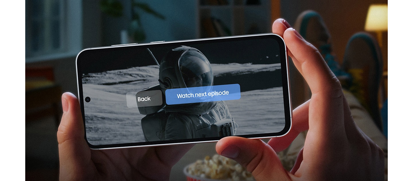 Two hands hold a Galaxy S23 FE device showing the end of a series onscreen. A subtitle reads watch next episode, back to highlight that the device has long-lasting battery. Text reads Listen up to 69 hours, Watch up to 22 hours.