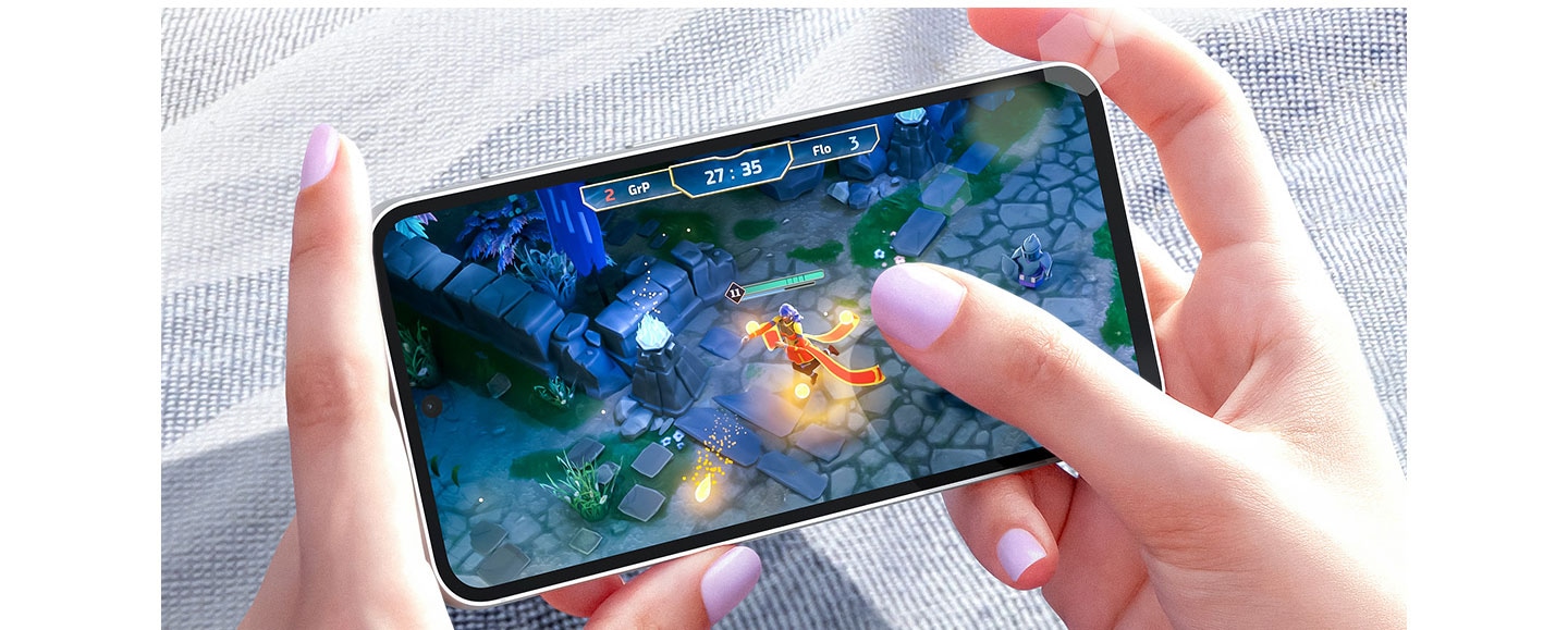 Two hands playing a video game on a Galaxy S23 FE device in bright daylight. The screen shows a clear image thanks to Vision Booster.