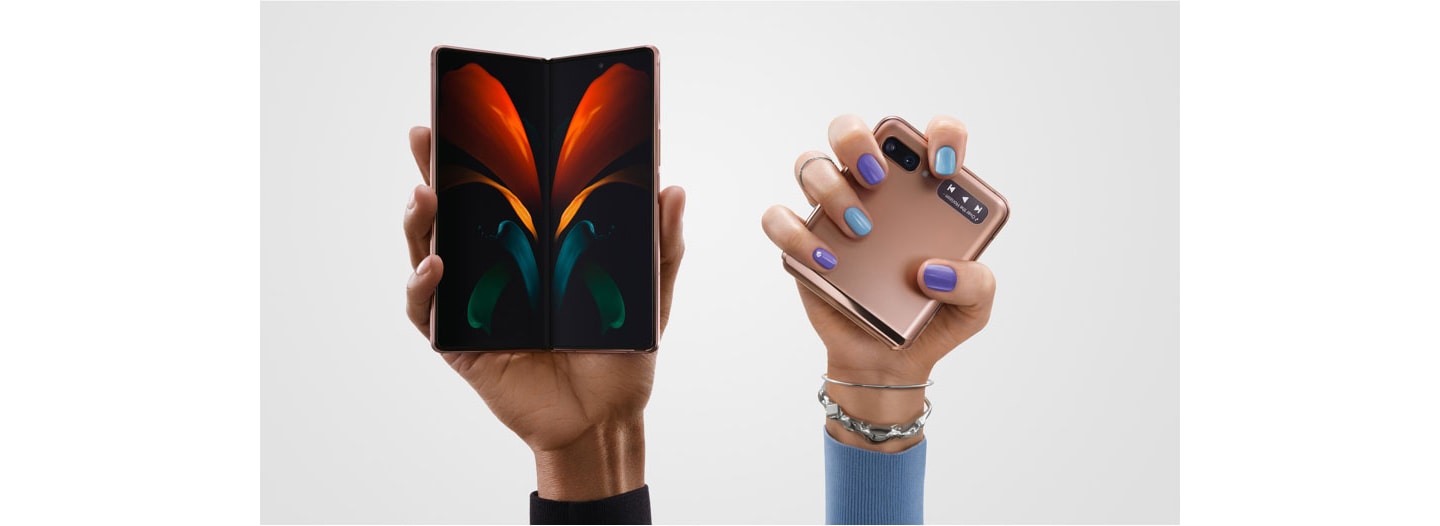 Two hands hold up two Galaxy devices. On the left, an open Galaxy Z Fold2 5G, open to the camera with a red, orange, blue and green butterfly design on it. On the right, a closed Galaxy Z Flip 5G.
