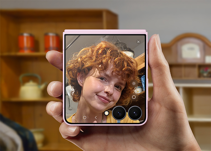 يدٌ تحمل هاتف Galaxy Z Flip8 مطوياً، تُظهر شخصاً ينظر إلى نفسه على شاشة الغطاء عبر ميزة عرض المرآة.
