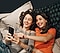 Two women lying down together smiling and looking at their smartphones.