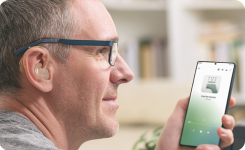 A person wearing a hearing aid and using a Galaxy S25.