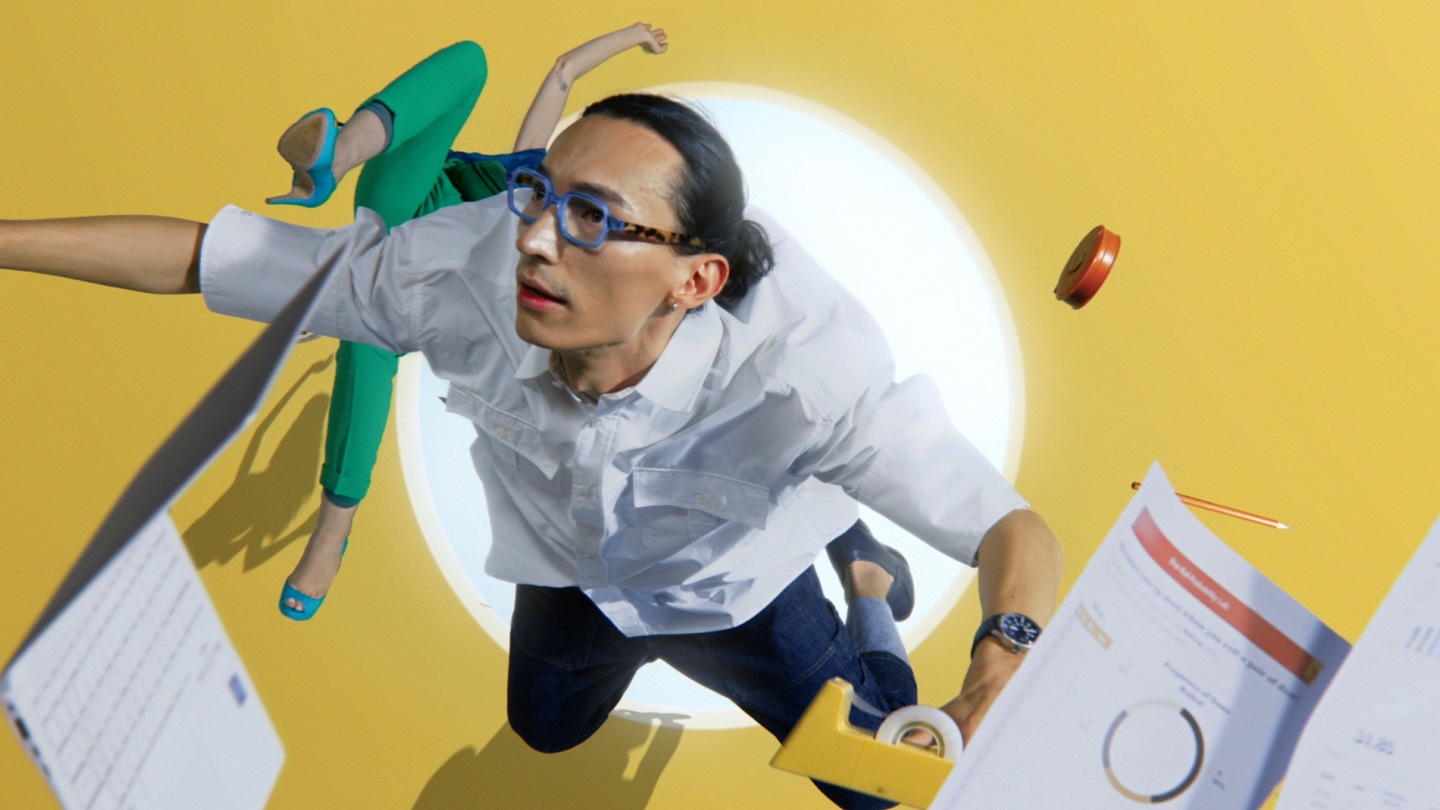 Une femme et un homme volent dans les airs avec un ordinateur portable, un crayon et des fournitures de bureau grâce au courant provenant d’un trou rond dans le mur jaune.