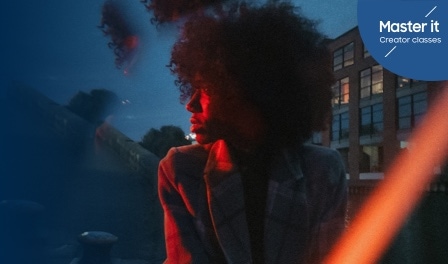 Une femme en veste regardant vers la gauche, subtilement illuminée par une lumière rouge devant un ciel bleu. Master it Creator classes