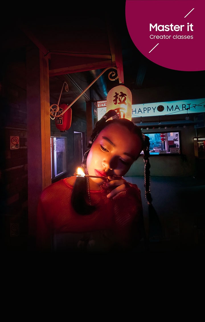 Une femme regarde une longue allumette qui brûle dans un marché aux couleurs néon. Master it. Creator classes.