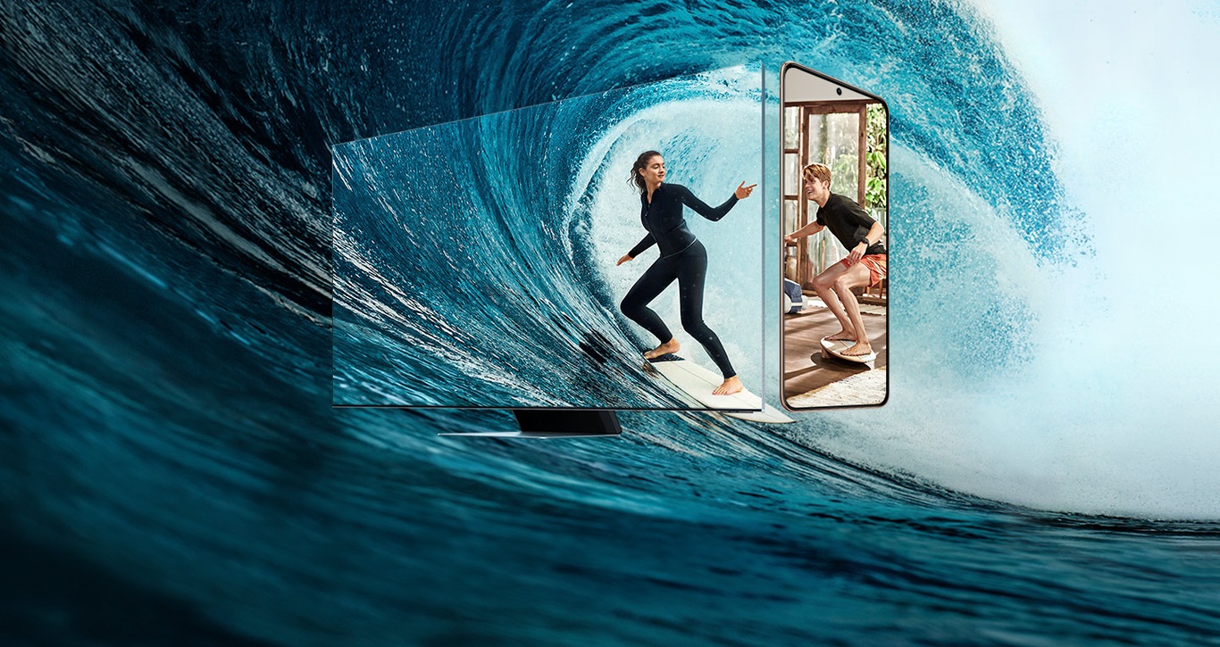 Samsung Smart TV and Galaxy S21 smartphone are placed side by side, with ocean waves in the background. Displayed on the TV is a woman surfing, while a man training on a balance board is shown on the phone, indicating the two are connected via Multi View