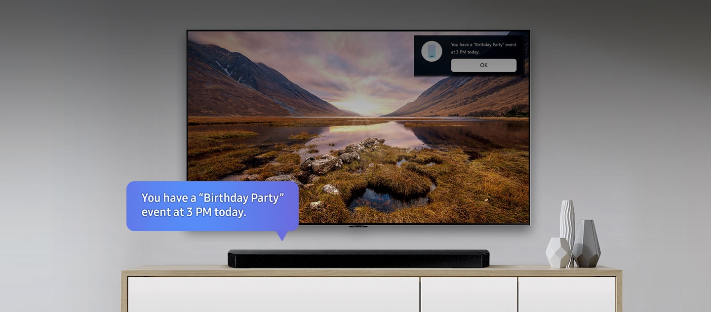 Uma TV Samsung ao centro e uma soundbar localizada abaixo dela. Um balão de texto azul na soundbar diz: "Tem um evento de "Festa de Aniversário" às 15:00 de hoje." No canto superior direito da TV é mostrada uma notificação com o mesmo lembrete e um botão “OK” abaixo.