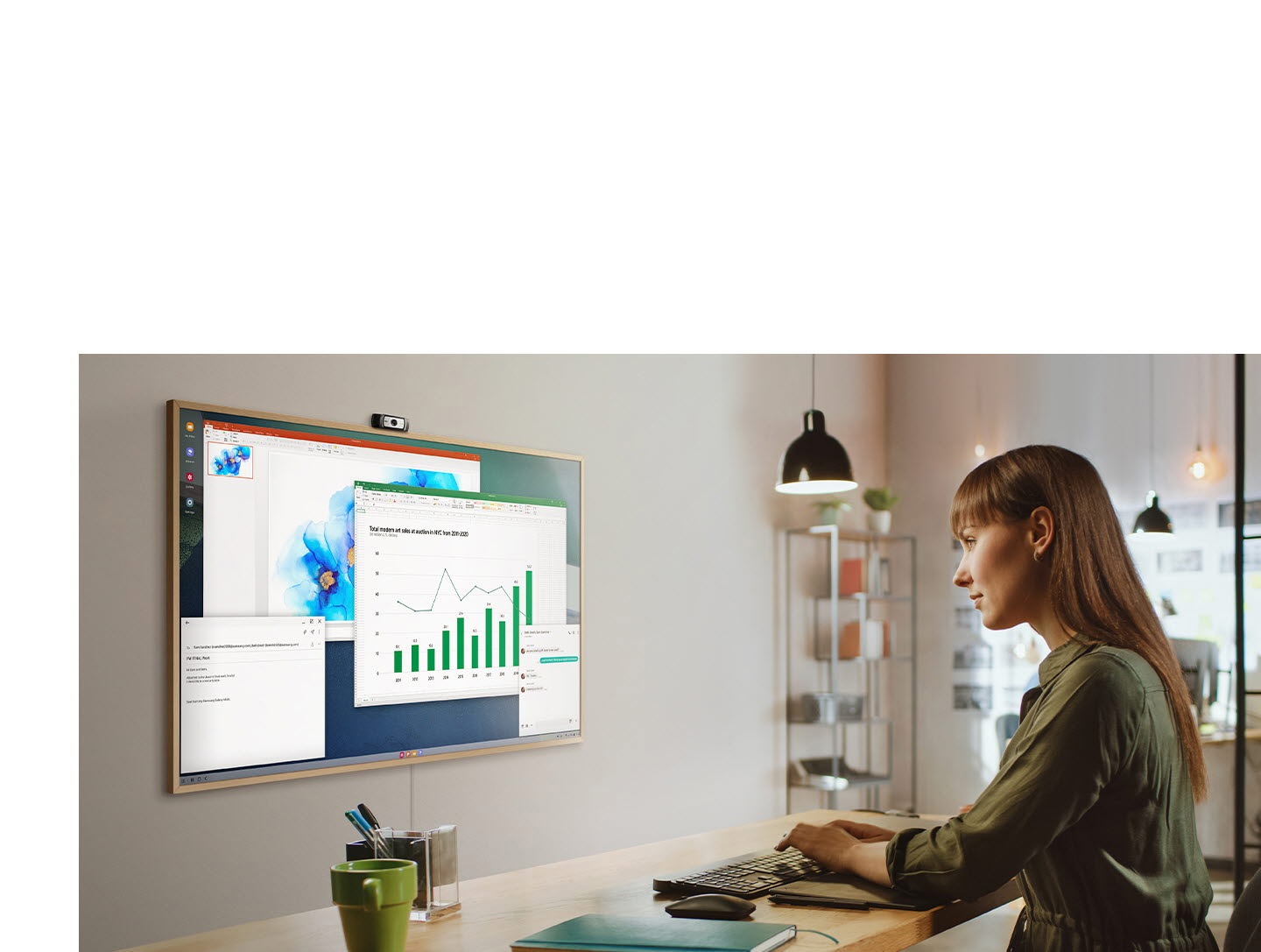 Una mujer utiliza la PC de su oficina para hacer trabajos en la pantalla de su televisor en casa. En la pantalla de The Frame hay varias ventanas de productividad de la oficina.