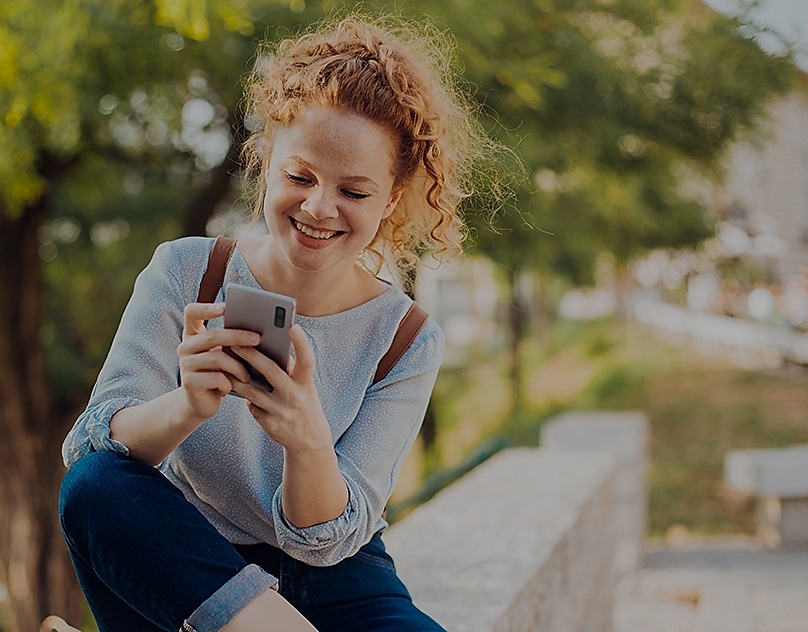 Eine junge Frau lächelt, während sie auf ihr Smartphone blickt.