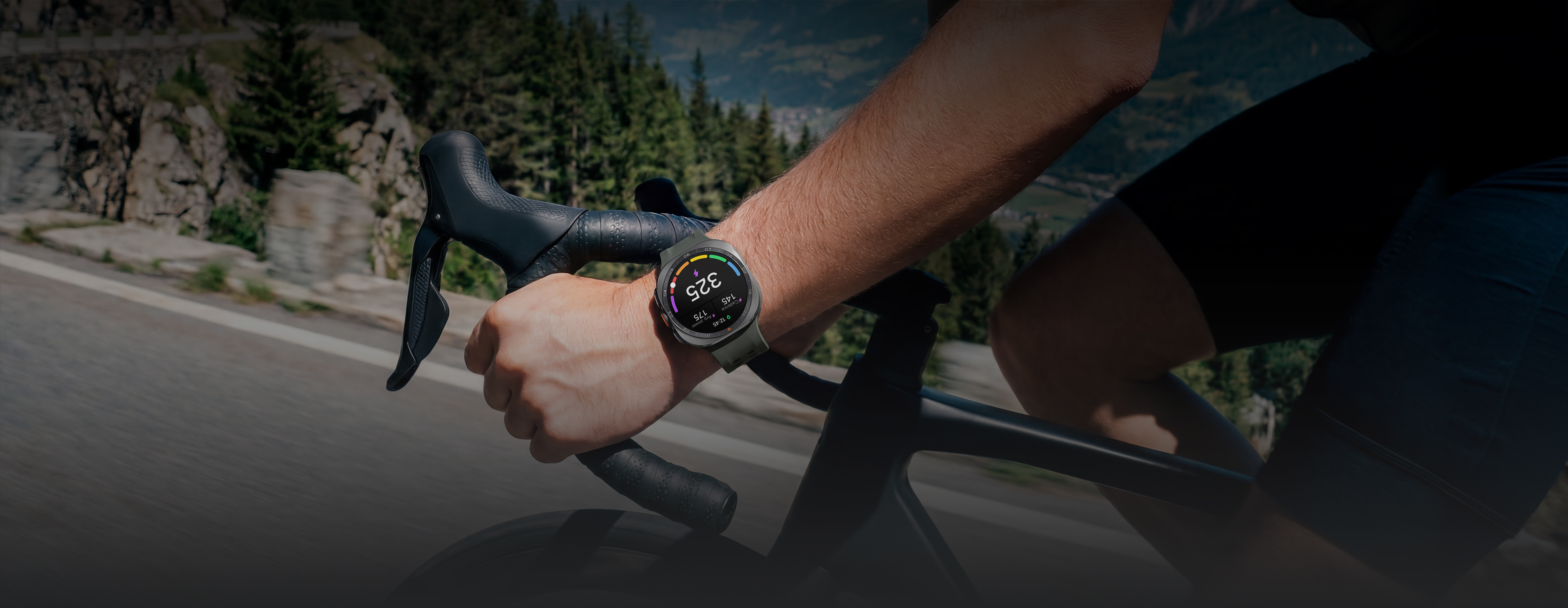 Eine Person auf dem Fahrrad ist auf einer Bergstraße unterwegs und trägt dabei eine Galaxy Watch Ultra2 in Titanium Silver mit einem Marine Band in Olive. Das Display zeigt die persönliche Funktionsleistungsschwelle (FLS) mit Trittfrequenz und Durchschnittsleistung.