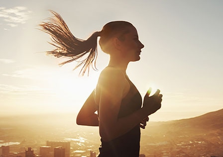 Une femme court avec le soleil levant en arrière-plan. Ses cheveux flottent dans le vent, montrant un mouvement dynamique.