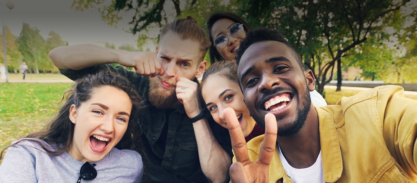Cinco pessoas sorrindo e tirando uma selfie juntas em um parque.