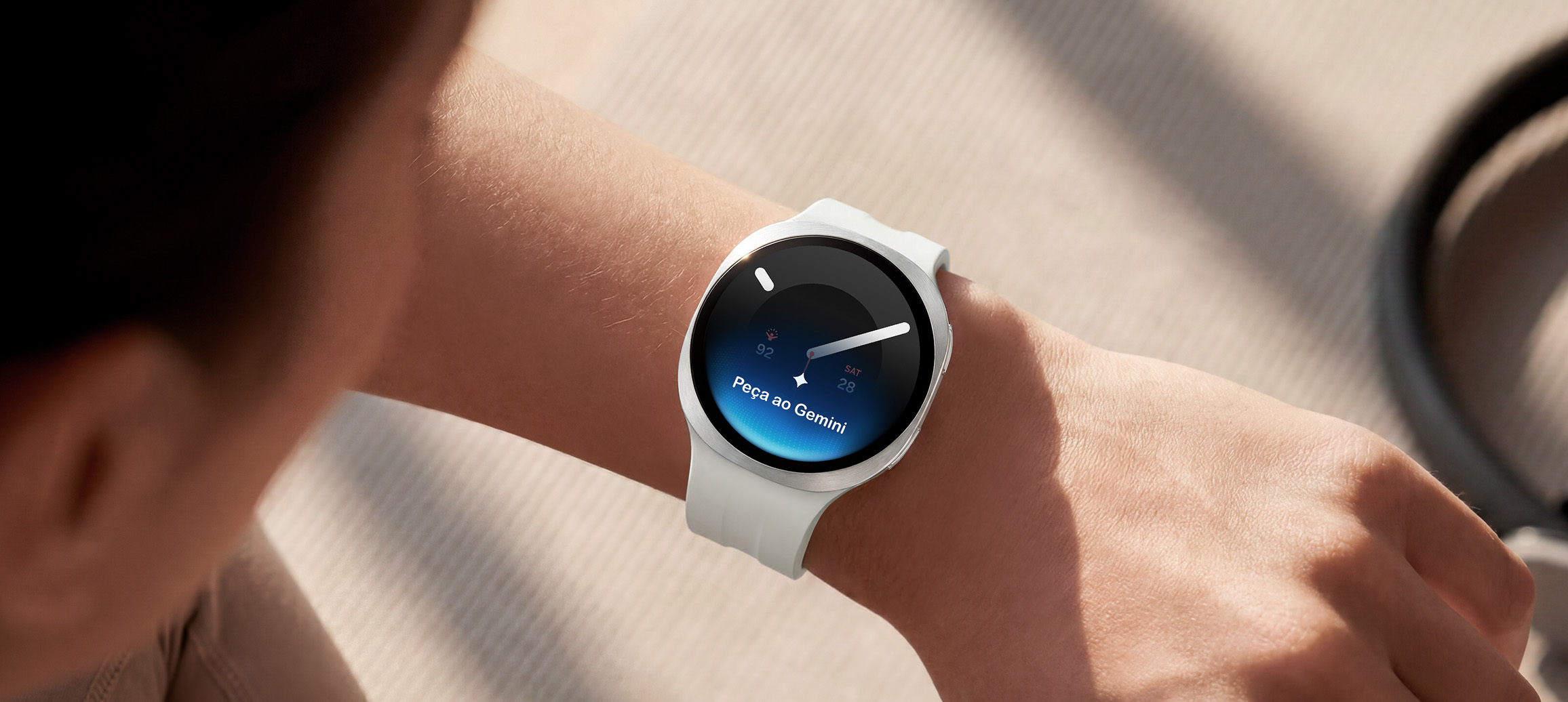 Uma pessoa usando o Galaxy Watch9 em Prata com uma Pulseira Sport em Cream levanta o pulso para dar um comando de voz ao relógio usando o Google Gemini. Ícone do Google Gemini e texto Pergunte ao Google Gemini mostrados na tela do relógio.