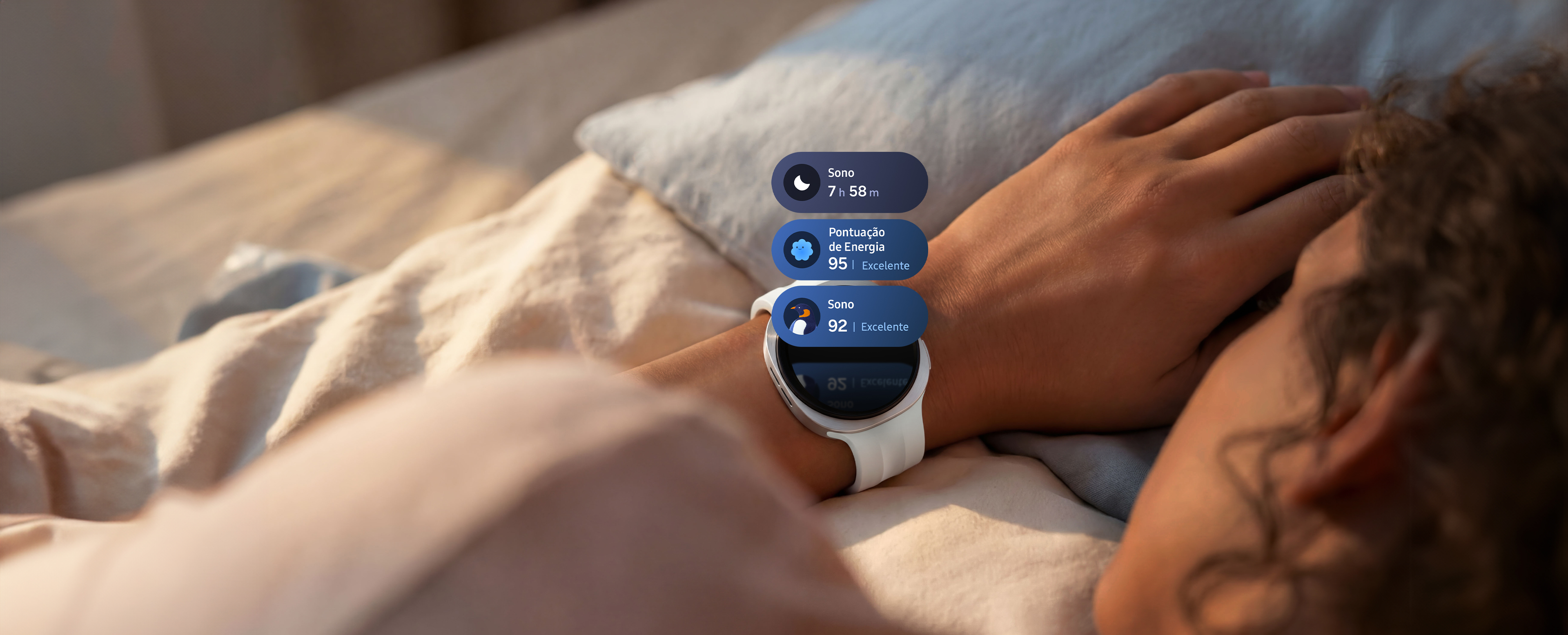 Galaxy Watch9 em Prata com uma Pulseira Sport em Cream usada no pulso de uma pessoa,'s com ondas de luz se espalhando do relógio ao longo do braço da pessoa's simbolizando o monitoramento do sono. Três blocos de monitoramento do sono aparecem acima da tela do relógio, incluindo um bloco com duração do sono de 7h58m, um bloco com um Pontuação de energia Excelente de 95 e um bloco de coaching de sono com um ícone de pinguim e uma pontuação de sono Excelente de 92.