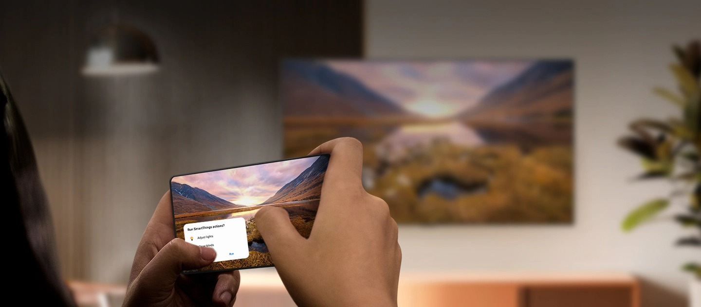 A Galaxy smartphone casting a majestic landscape image onto a Samsung TV in the background. The TV displays the identical landscape image.