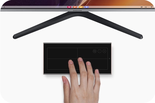 A Samsung TV with Samsung DeX onscreen wirelessly connected to a Galaxy Note20 Ultra, which is laying in landscape mode in front of the TV while a person uses it as a touchpad.