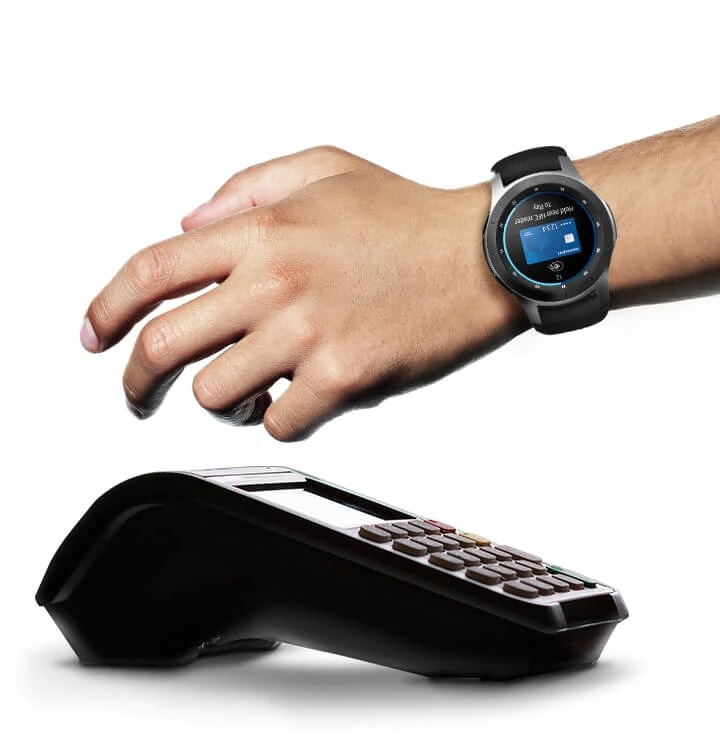 Galaxy Watch Watch ke pergelangan tangan kiri dengan tangan yang diletakkan di atas titik terminal jualan. Dail itu dilihat dari depan dengan skrin yang menunjukkan permohonan Samsung Pay dalam proses menjalankan transaksi