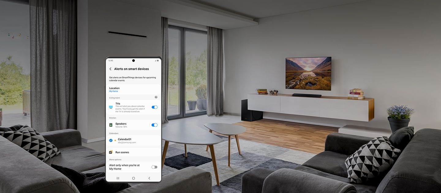 En arrière-plan, l’intérieur d’un salon épuré avec des canapés, une télévision et d’autres éléments. Au premier plan, un smartphone Galaxy montre le menu des paramètres «Alertes sur les appareils intelligents».