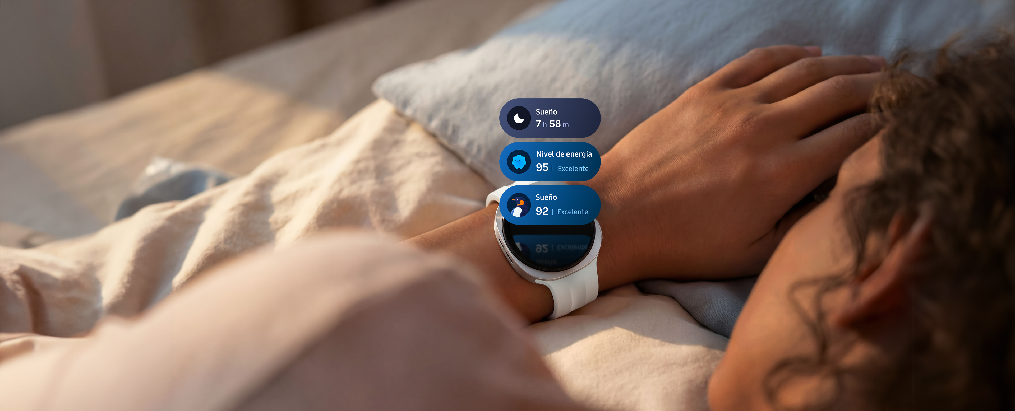 Galaxy Watch9 en Silver con una correa deportiva en Cream, puesto en la muñeca de una persona', con ondas de luz que se desplazan desde el reloj a lo largo del 'brazo de la persona para indicar el seguimiento del sueño. Sobre la pantalla del reloj aparecen tres ventanas de seguimiento del sueño, que incluyen una ventana con una duración de sueño de 7 h 58 m, una ventana con un excelente Energy score de 95 y una ventana de entrenamiento del sueño con un ícono de pingüino y una excelente puntuación de sueño de 92.