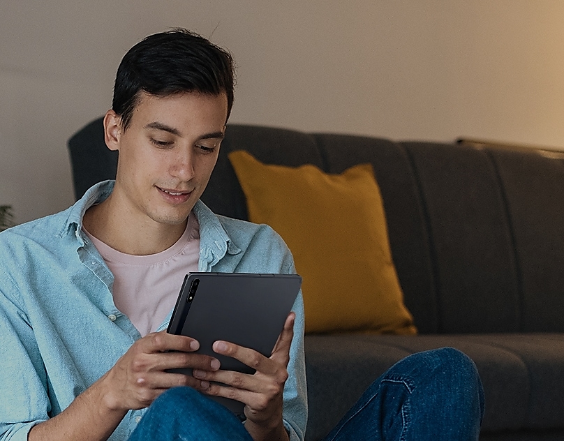 Ein Mann lächelt, während er auf sein Galaxy Tablet blickt.