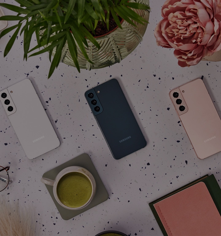 4 Samsung Galaxy S22 Smartphones in den Farben Phantom White, Phantom Black, Green und Pink Gold liegen mit dem Display nach unten auf einem Tisch.