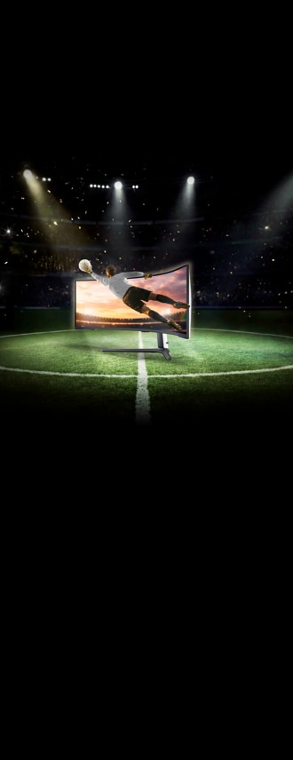 Gebogener Samsung Monitor zeigt springenden Fußballspieler in Trainingsszene, platziert auf grünem Rasen im beleuchteten Stadion.