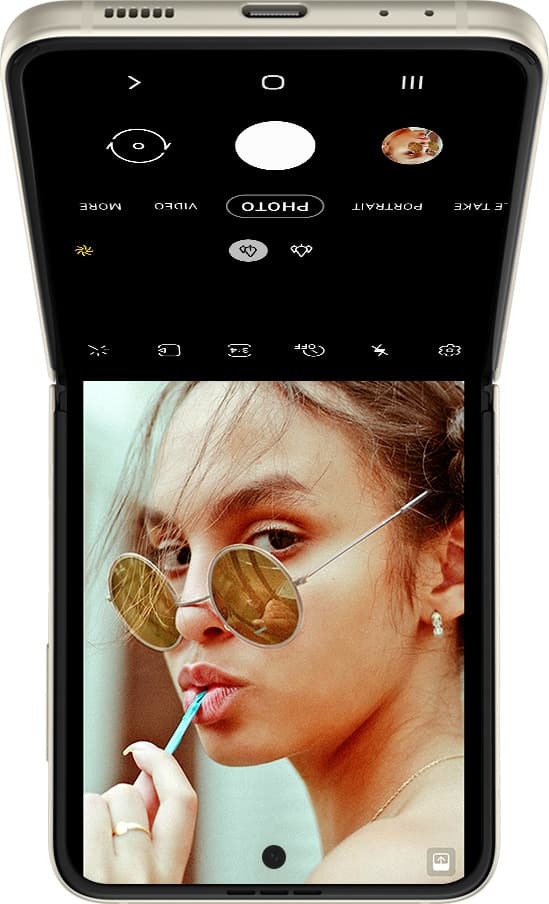 Ein auf dem Kopf stehendes Galaxy Z Flip3 5G im Flex-Modus mit der Benutzeroberfläche der Kamera auf dem Hauptbildschirm. Das Gesicht einer Frau ist im Sucher zu sehen.
