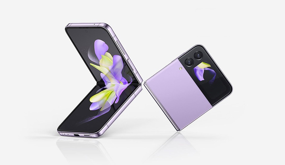 Zwei Galaxy Z Flip4 in Bora Purple liegen nebeneinander. Das eine ist in einem 90-Grad-Winkel geöffnet und sein Hauptdisplay zeigt ein lila-gelbes bandähnliches Hintergrundbild. Das andere ist zusammengeklappt und sein Frontdisplay zeigt das gleiche Hintergrundbild wie das Hauptdisplay des anderen Geräts.