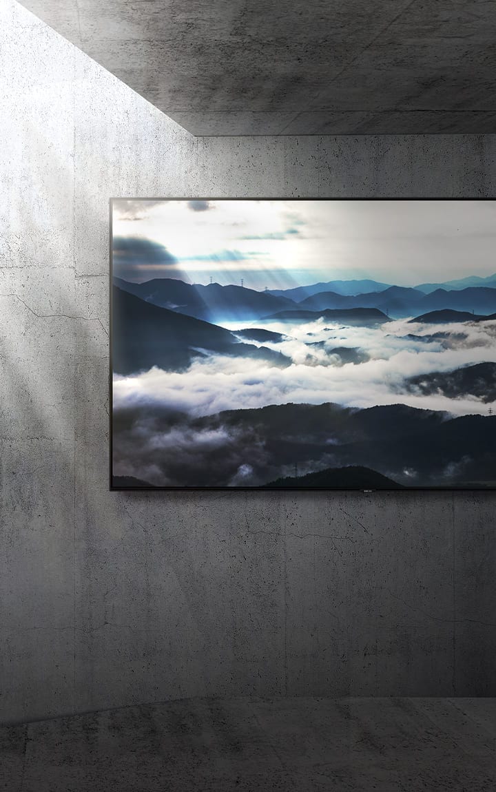 Ein großes TV-Gerät, das an einer Beton-Wand angebracht ist, zeigt eine Landschaftsszene in 4K-Auflösung, während von links Sonnenlicht ins Bild fällt. 