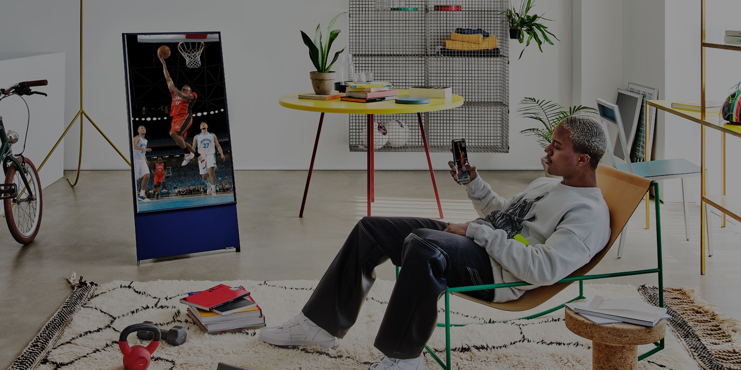 Ein Mann verbindet ein Samsung-Smartphone mit einem Samsung-Fernseher und nutzt die Smart View-Bildschirmspiegelung, um ein Basketballspiel auf beiden Bildschirmen zu sehen