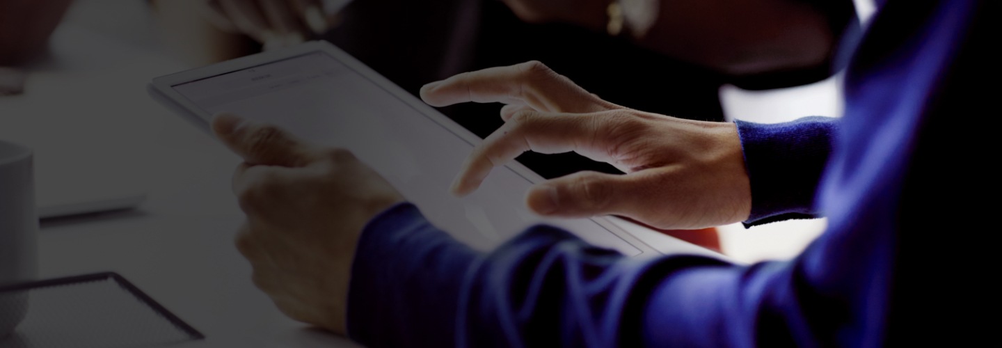 Close-up view of a person's hands. The person is holding a tablet in his left hand and scrolling through a document on the screen with his right index finger.