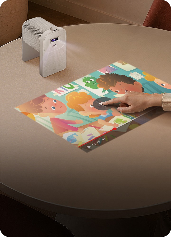 Le projecteur interactif The Premiere 5 de Samsung projette une vidéo pour enfants sur une table de salle à manger. Une personne appuie sur le bouton de lecture directement sur la table pour afficher le contenu.